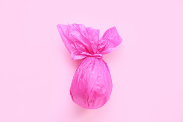 Chocolate Easter egg wrapped in pink paper on color background