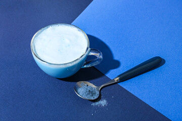 Fototapeta na wymiar Cup of delicious matcha tea and spoon with powder on blue background