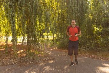 Portrait of a man running in a park. Close up of a smiling man running while listening to music using earphones