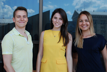 Portrait of the happy young man and two women posing near the glass-facade building