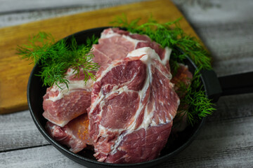 Close-up photo of cuts of meat with dill greens and spices in a steak pan on wooden table and cutting board.