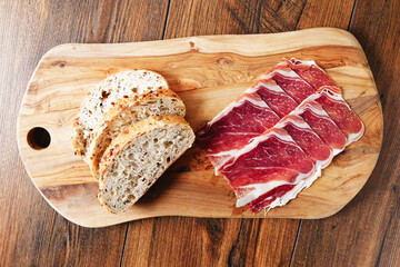 Premium Spanish dry cured ham on a wooden board and wooden background and a slice of bread . Top quality meat product.