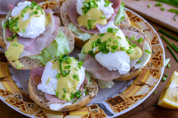 Sandwiches with poached egg, ham, lettuce, and chives, topped with sauce. Eggs Benedict