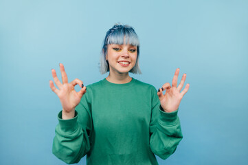 Joyful hipster lady with colored hair with a smile on her face stands on a blue background and...