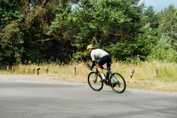A man in outfit trains on a bicycle in the woods on an asphalt road, quickly rides forward, side view.