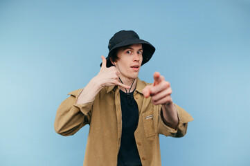 Handsome young man in casual clothes and panama stands on a blue background and shows his finger to...