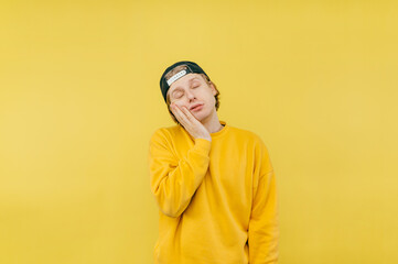 Tired guy in a cap sleeps on a yellow background on his arm with his eyes closed, isolated