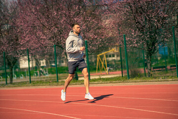Obraz premium A man in a gray hoodie is jogging at a sports stadium.