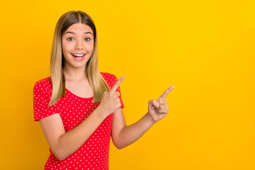 Portrait of surprised funny girl indicate two fingers empty space promo isolated on yellow color...