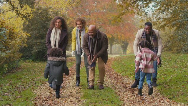 Portrait of smiling multi-generation family walking through autumn countryside together with grandchildren running to parents who pick them up and throw them in the air - shot in slow motion