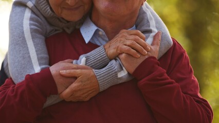 Aged Caucasian woman hugs her husband from the back holding hands together portrait selective focus on hands no faces visible selective focus closeup. High quality photo