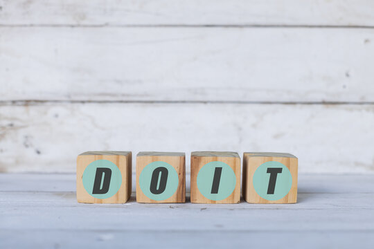 doit concept written on wooden cubes or blocks, on white wooden background.