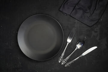 Empty black slate plate on dark stone table. Food background for menu, recipe. Table setting. Flatlay, top view. Mockup for restaurant dish	