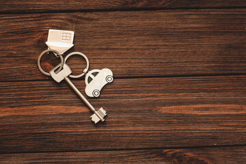 The key to the apartment with a keychain in the shape of a house and car on wooden background.