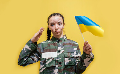 Ukrainian girl kid in military uniform with a dirty face, salutes. Child against war