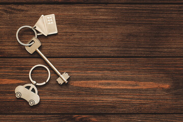 The key to the apartment with a keychain in the shape of a house and car on wooden background.