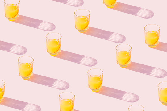 Orange juice drinks on a pastel pink background. Aesthetic juicy drink concept with long shadow glasses.