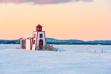 Naklejka premium Winter's view of the little lighthouse of Saint-Andre-de-Kamouraska with ice on Saint-Lawrence river and the Charlevoix in background (Quebec, Canada).