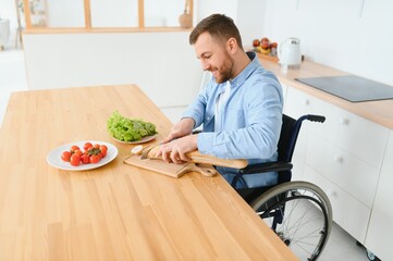 Young Disabled Man Sitting On Wheel Chair Preparing Food In Kitchen