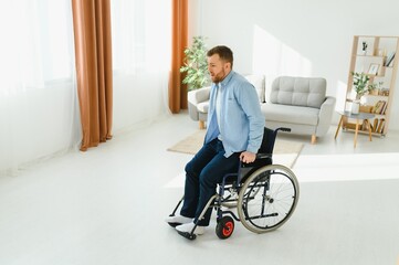 young man trying to get up from wheelchair at home, full length. Impaired black man attempting to stand, exercising his legs indoors, copy space