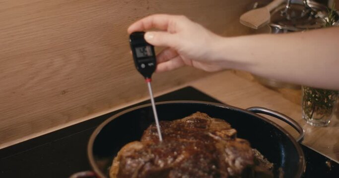 Female cook measures beef steak temperature close up hand thermometer
