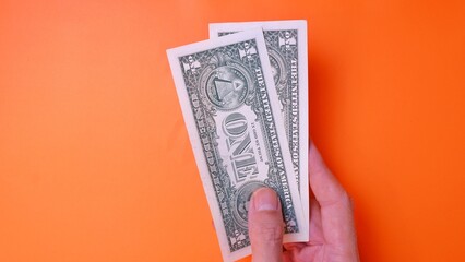 Man's hand is making a payment. Business Investment Economy Saving Loan Income Money and Finance concept. Male hand showing dollar cash on an orange background. One Dollar 1 USD. Prosperity concept.