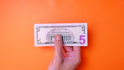 Man's hand is making a payment. Business Investment Economy Saving Loan Income Money and Finance concept. Male hand showing dollar cash on an orange background. Five Dollar 5 USD. Prosperity concept.