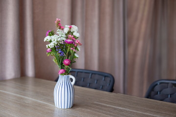 Striped vase with white and pink chrysanthemums stands on wooden table on the curtain background