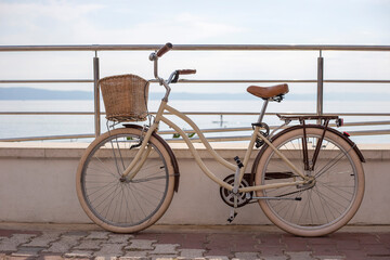 White women's bicycle with wicker basket stands on the beach background in summer