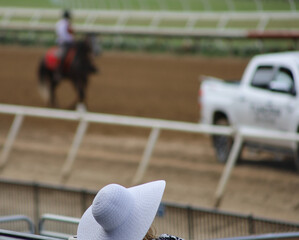 View of a woman with a white derby hat at the horse races with depth of field, background.