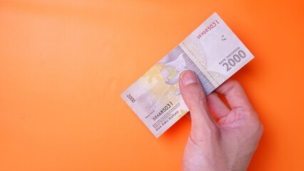 Indonesian Rupiah the official currency of Indonesia. Man's hand is making a payment. Male hand showing Indonesian Rupiah note. Business Investment Economy and Finance concept. Uang 2000 2.000 Rupiah