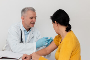 Fototapeta premium Female patient looking at her arm while doctor in protective gloves is injecting flu vaccine