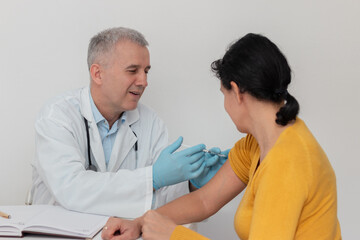 Fototapeta premium Female patient looking at her arm while doctor in protective gloves is injecting flu vaccine