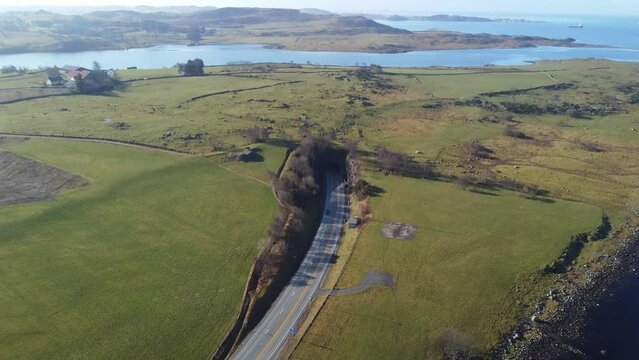 Subsea byfjord tunnel in Stavanger Norway - Aerial approaching and decending towards entrance in sunny weather and surrounded by green grasslands