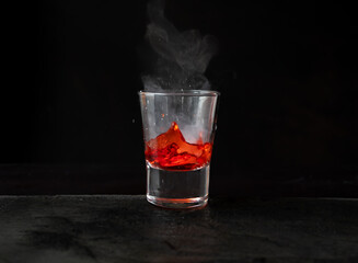 chapoteo de bebida con reacción química por hielo seco, con líquido rojo sobre piedra y fondo negro