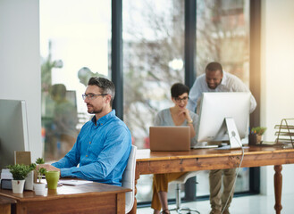 Focused on the tasks at hand. Shot of a businessman working in the office with two colleagues in the background.