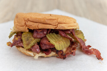 Tempting calorie filled pastrami sandwich garnished with sliced pickles on a bun and ready to eat