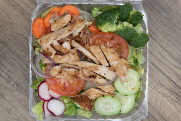 Overhead view of take out order of grilled chicken salad in a clear plastic container for convenient eating