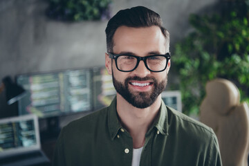 Photo of positive cheerful young man wear green shirt spectacles smiling indoors workshop workplace...