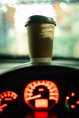 Coffee cup on car console during the rainy morning. Rush hour in the city concepts.
