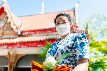 Buddhist woman holding incense sticks, candles, lotus flowers and masks to protect against Covid-19 at Buddhist ceremonies
