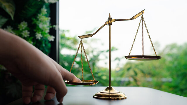 Tip the scales of justice concept as a the hand of a person illegally influencing the legal system for an unfair advantage.
