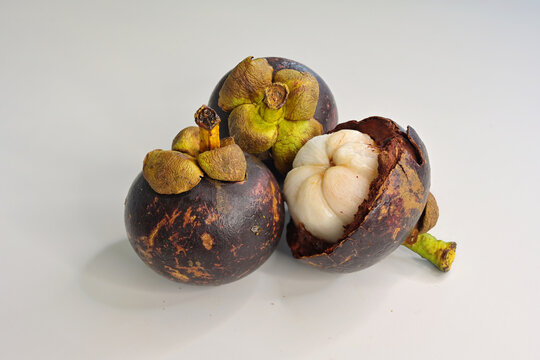 Half of an open mangosteen (Garcinia mangostana) and 2 ripe whole fruits on white background