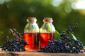 Elderberry syrup in a glass bottle and bunches of elderberries on a wooden table in the summer...
