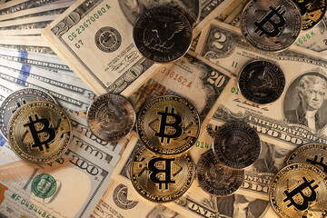 Bitcoin coins on top of US Dollar banknotes and coins.