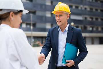 Real estate developer and master builder shaking hands while standing in construction site.