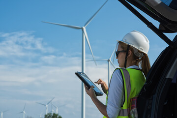 Service engineers woman Checking tablet against cars on wind turbine farm background. renewable ennergy ,sustainable concept. wind turbine installation.