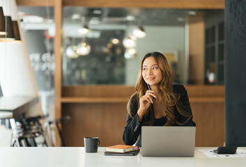 Portrait of dreamy lovely accountant sitting at desk in modern office with interior drinking hot beverage holding cup with tea in hands looking at window enjoying freetime