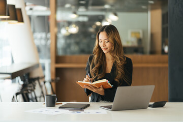 Business asian woman taking note on note book, Attractive girl working with laptop computer