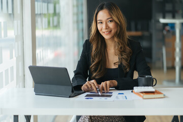 Fototapeta premium Young business woman sitting at her desk in an office, working on a laptop computer